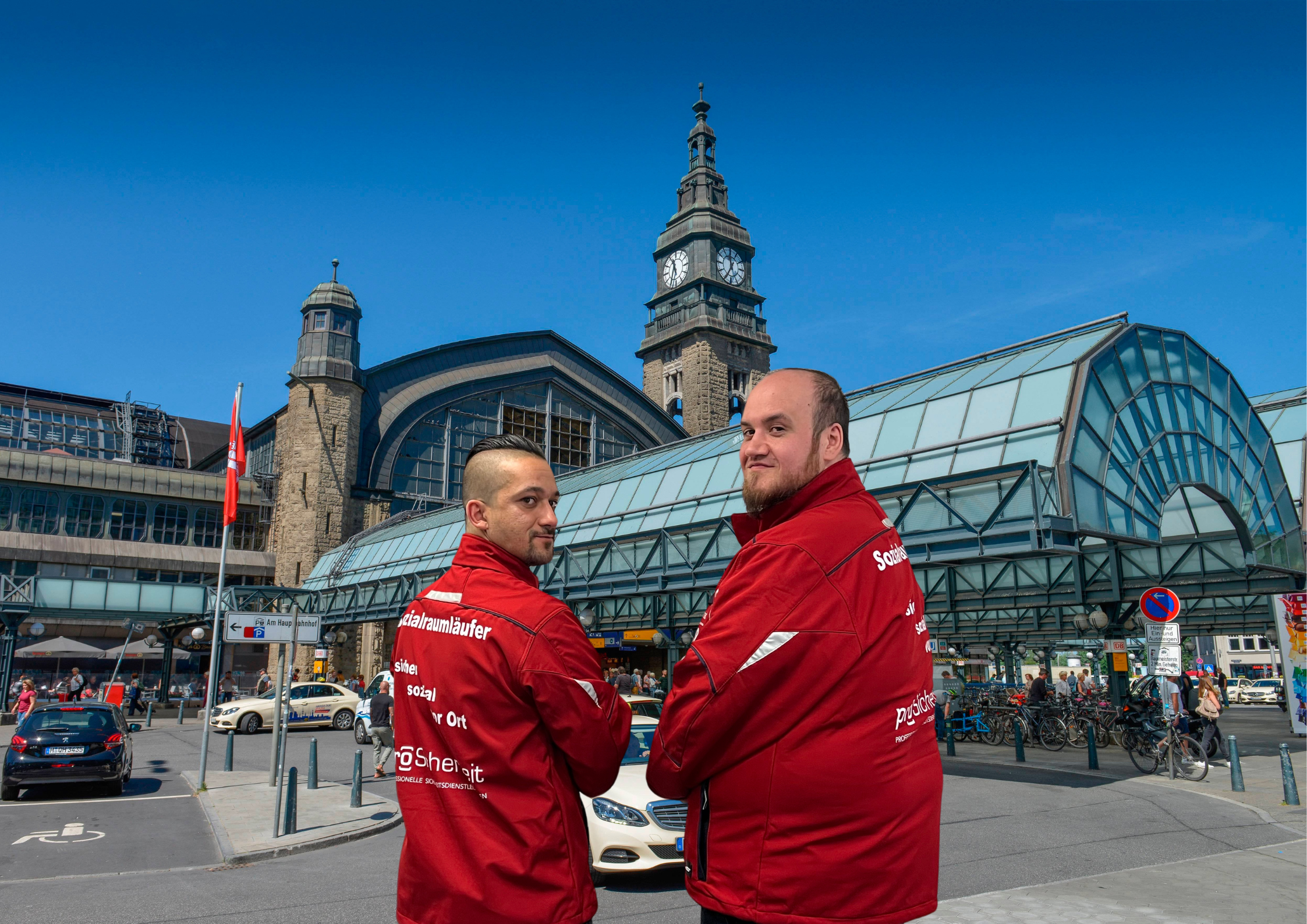 Die Sozialraumläufer Kevin (l.) und Karsten stehen vor dem Hauptbahnhof, sie tragen rote Jacken.