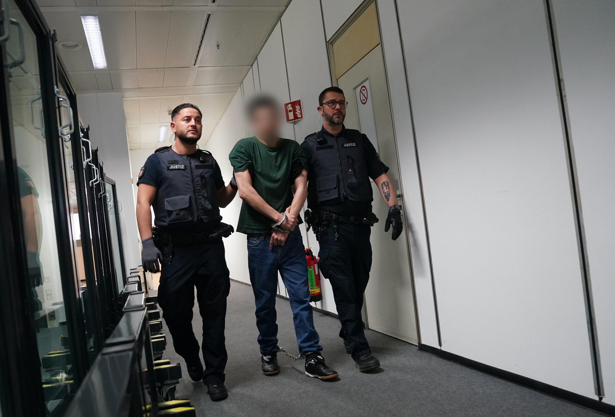 Zwei Justizvollzugsbeamte bringen den Angeklagten Ibrahim A. (M.) in Hands- und Fußschellen in den Gerichtssaal im China Logistic Center gebracht.