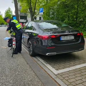 Ein Polizist untersucht das Fahrrad der verunglückten Frau, daneben auf dem Parkstreifen steht eine schwarze Mercedes-Limousine.