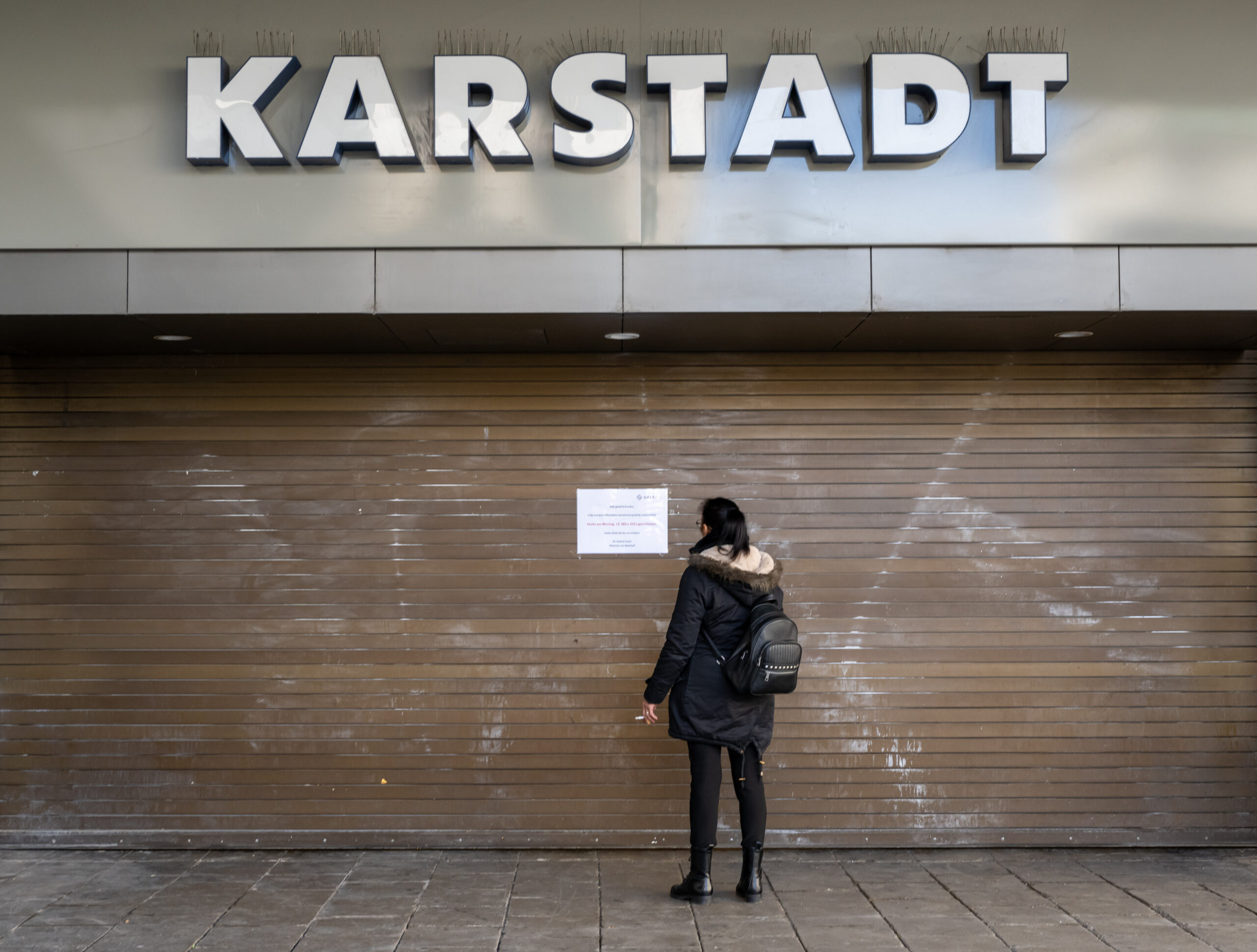 Eine Passantin steht vor einem geschlossenem Eingang der Karstadt-Filiale am Hauptbahnhof München.