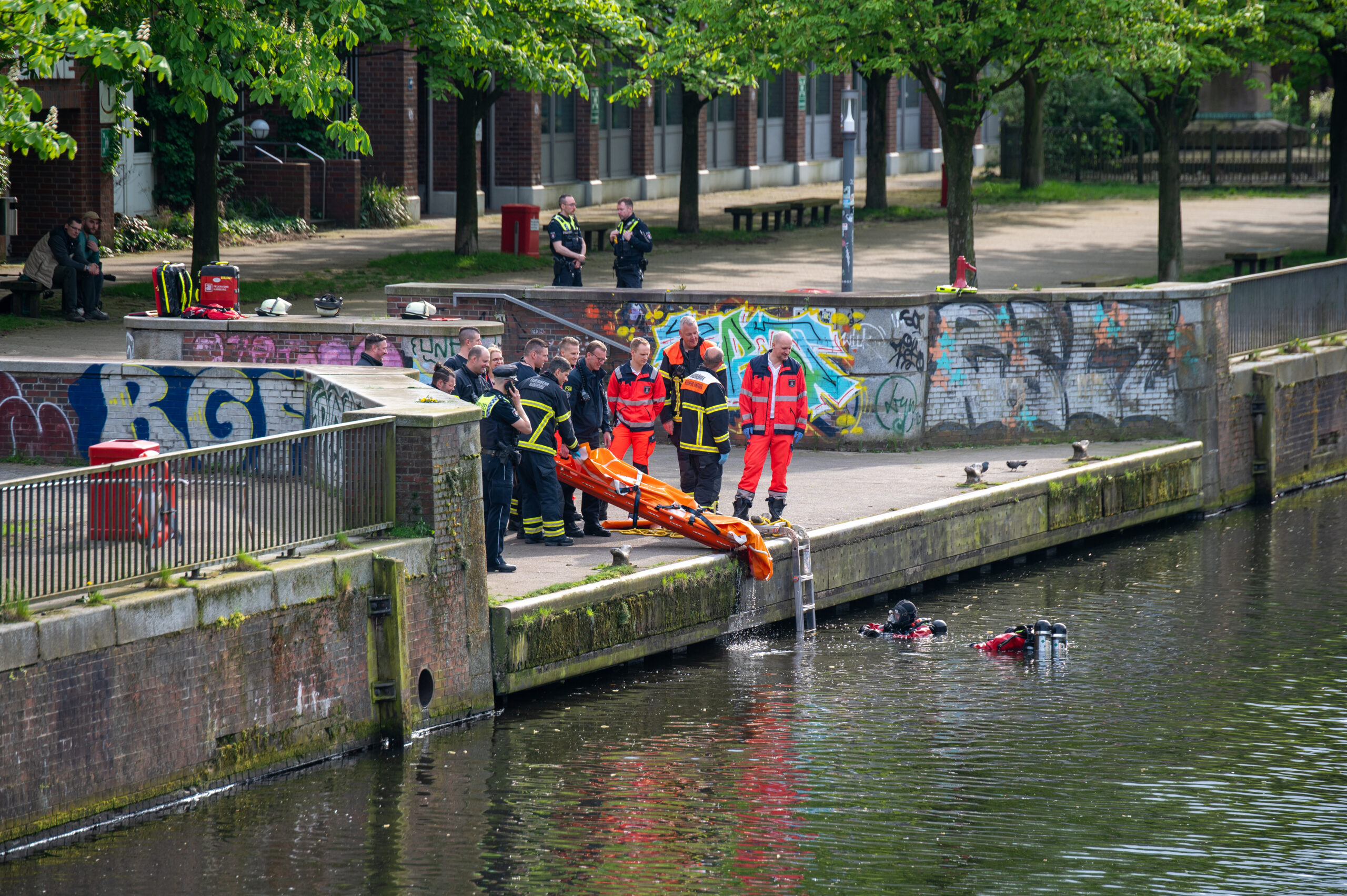 Einsatzkräfte der Polizei und Feuerwehr stehen am Ufer des Mittelkanals, wo zuvor eine leblose Person gefunden wurde.
