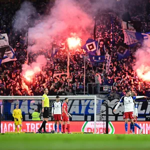 Auf der Nordtribüne im Volksparkstadion brennt Pyrotechnik, davor stehen HSV- und Kiel-Profis auf dem Platz