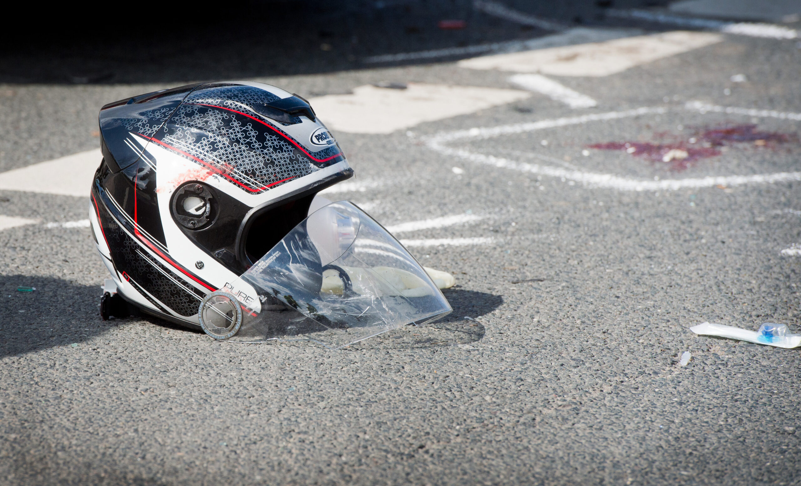 Ein beschädigter Motorradhelm liegt nach einem schweren Unfall zwischen einem Motorrad und einem Auto auf einer Straße. (Symbolfoto).