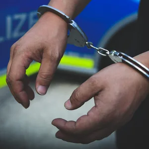 Hände in Handschellen vor Polizeiwagen