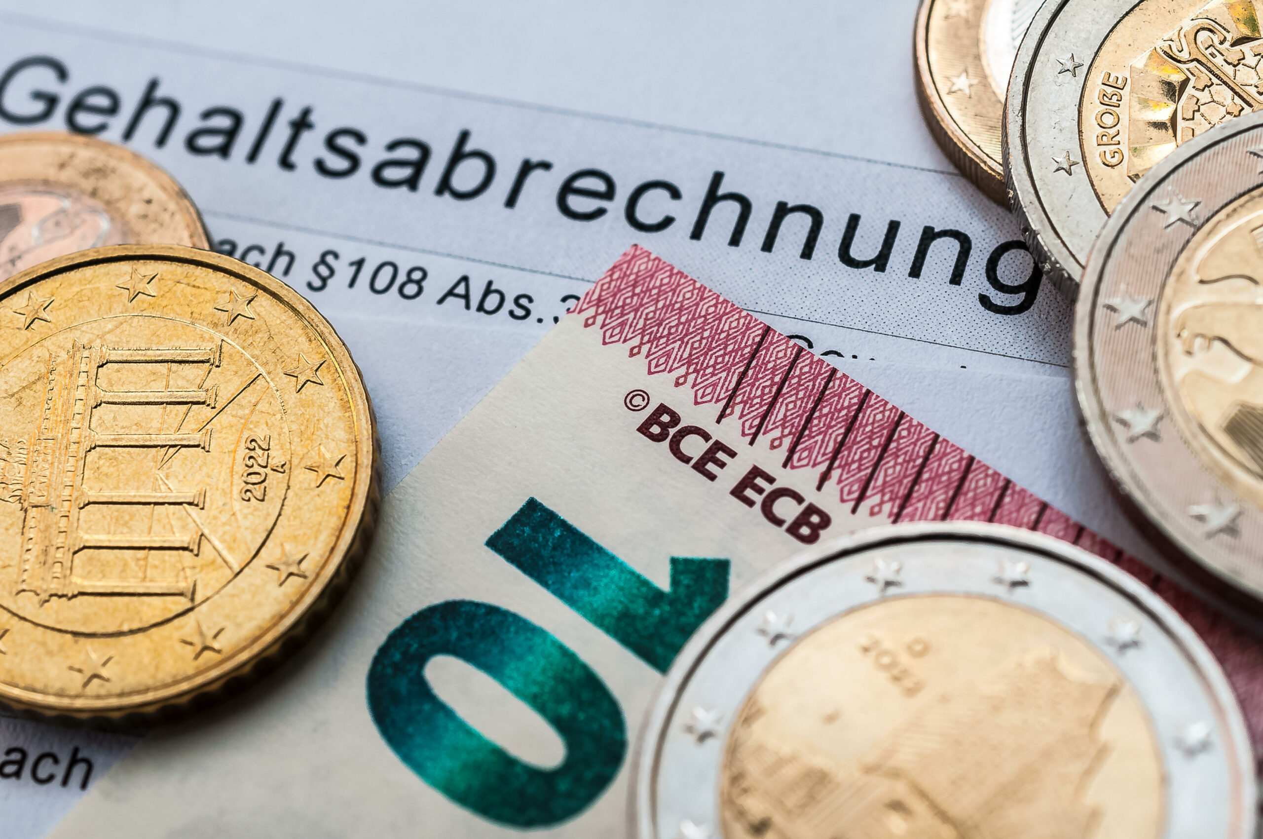 Geld – Münzen und ein 10-Euro-Schein – liegt auf einer Gehaltsabrechnung (Symbolbild).