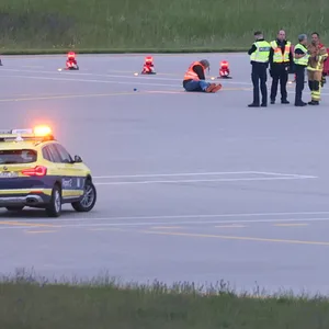 Einsatzkräfte von Polizei und Feuerwehr stehen auf einer Zufahrt für Start- und Landebahnen am Flughafen Franz-Josef-Strauß um Klimaaktivisten die sich dort festgeklebt haben.