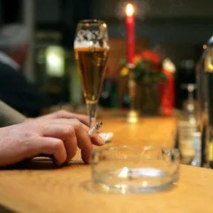 Ein Bier steht auf einem Tresen. Daneben ist eine Männerhand mit Zigarette zu sehen. (Symbolfot)
