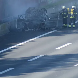 Feuerwehrleute löschen das brennende Auto.