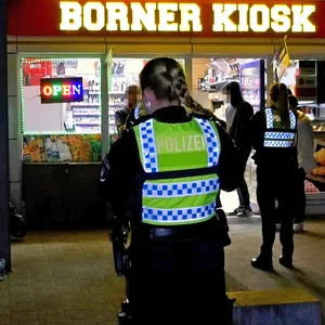 Polizisten stehen vor dem Kiosk und sprechen mit Zeugen.