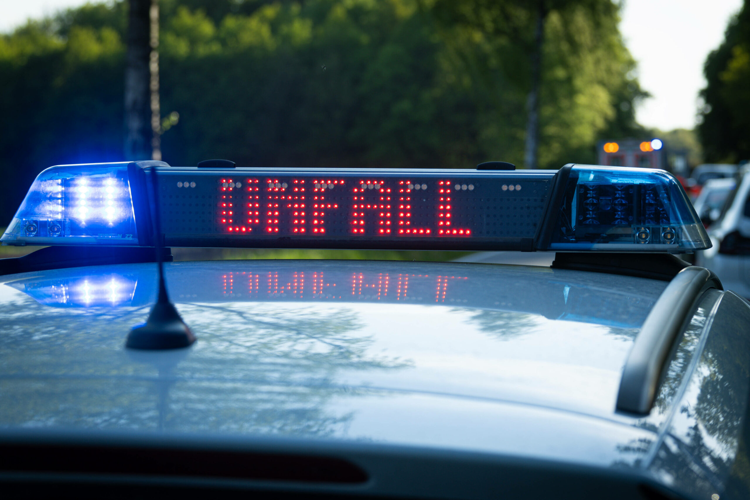 Ein Streifenwagen der Polizei steht mit Blaulicht und dem Schriftzug „Unfall“ im Display an einem Unfallort.