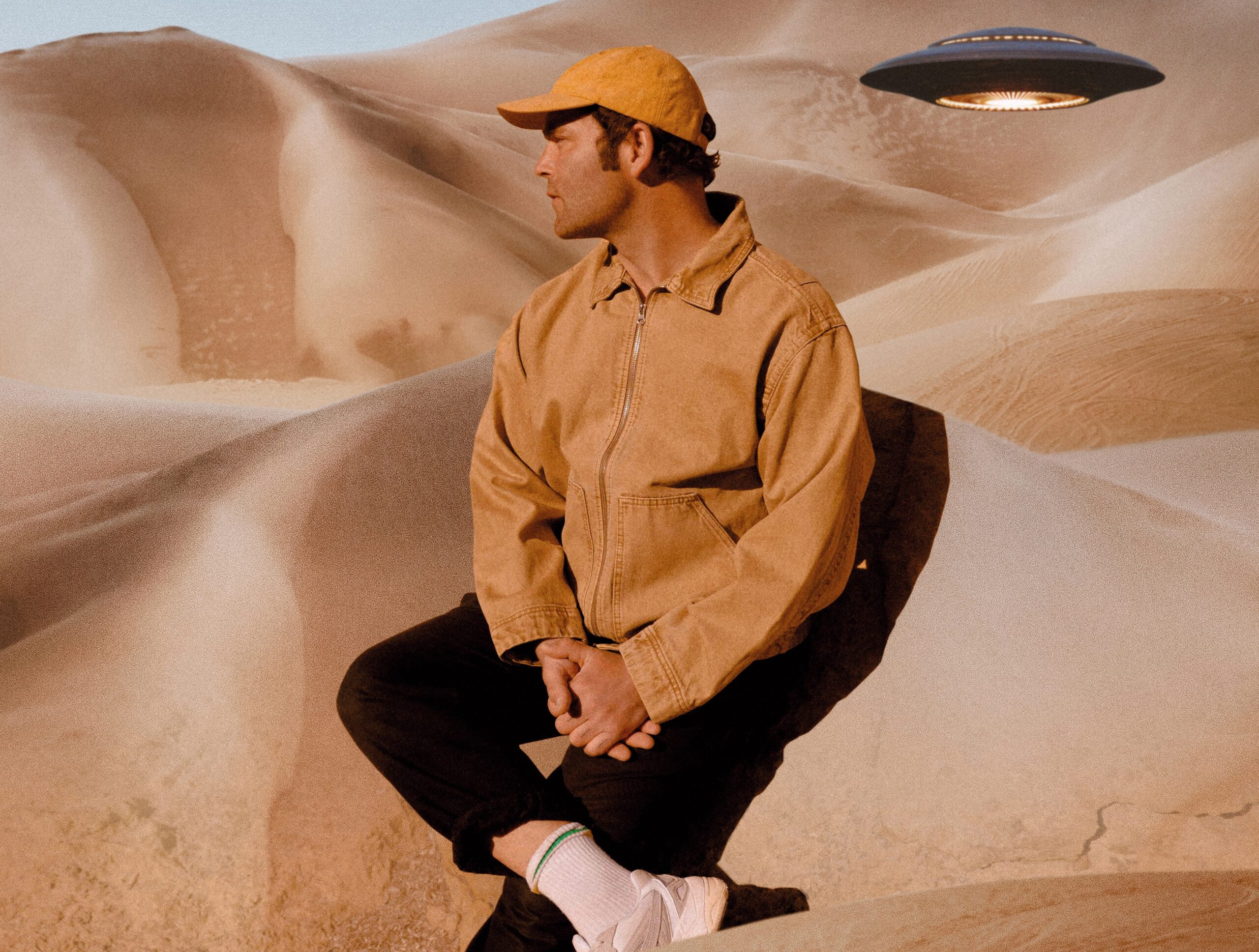 Bosse. Er scheint in einer Wüste zu sitzen, neben ihm schwebt ein UFO.