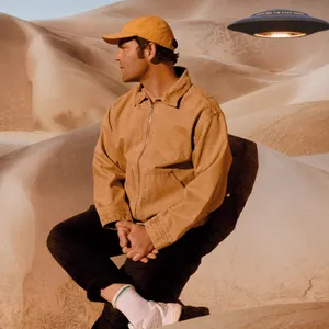 Bosse. Er scheint in einer Wüste zu sitzen, neben ihm schwebt ein UFO.