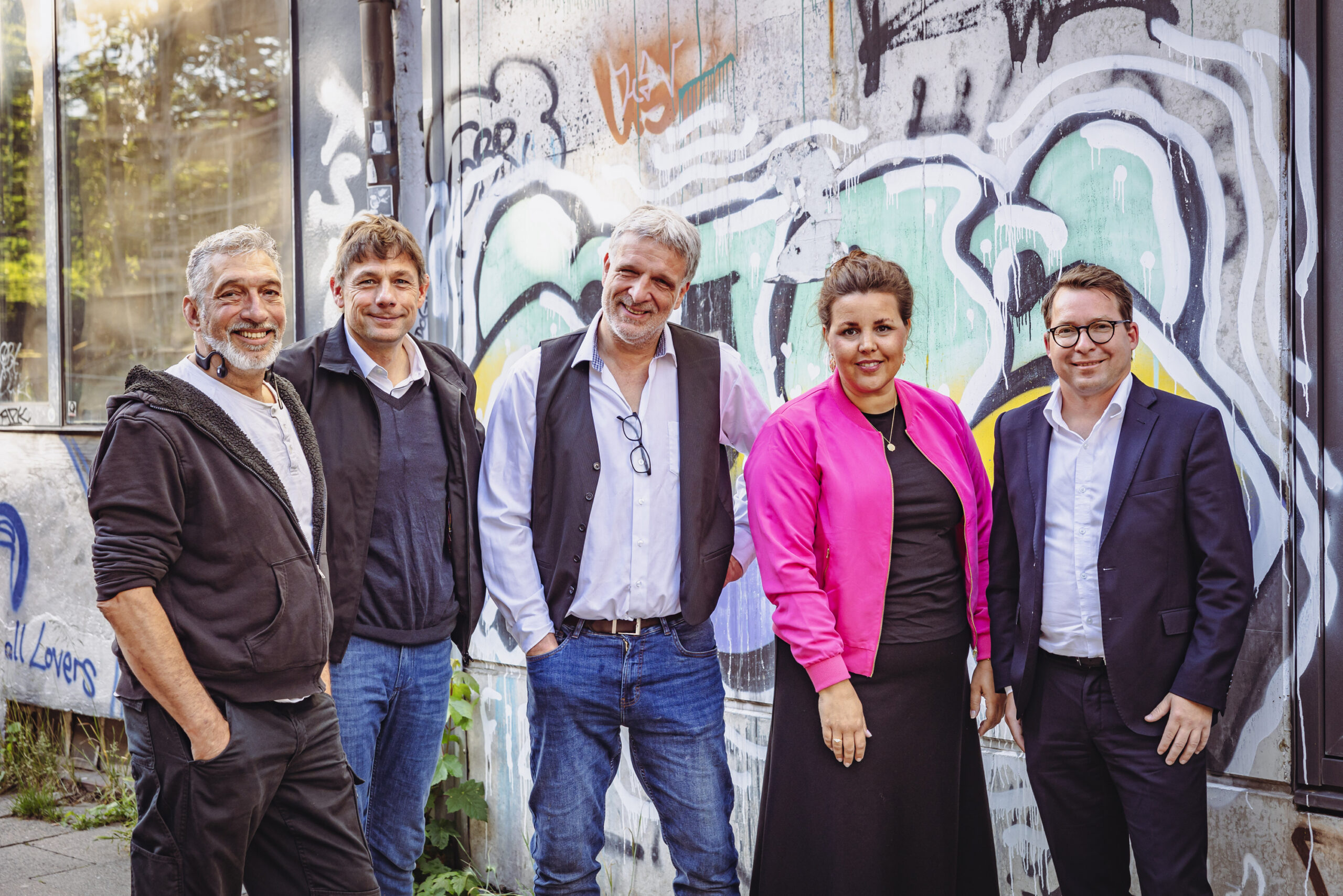 Gruppenbild: Vier Männer und eine Frau mit pinkem Blouson