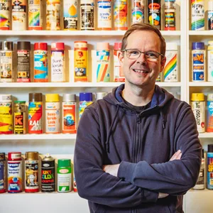 Mirko Reisser steht vor einem Regal mit vielen bunten Farbdosen