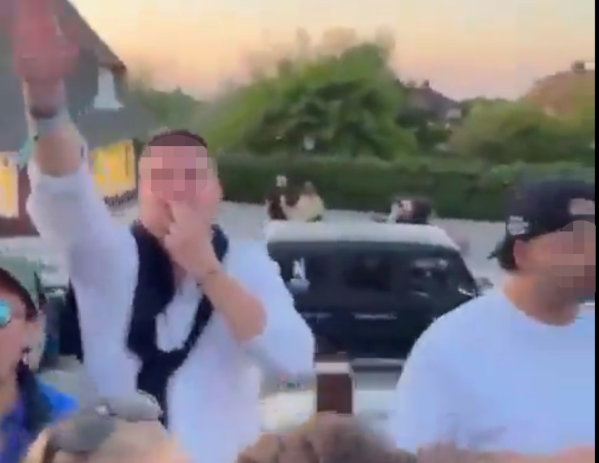 Ein Mann deutet mit seinen Fingern einen Hitlerbart an, während er den verbotenen Hitlergruß zu zeigen scheint – und grölt dabei „Deutschland den Deutschen, Ausländer raus“