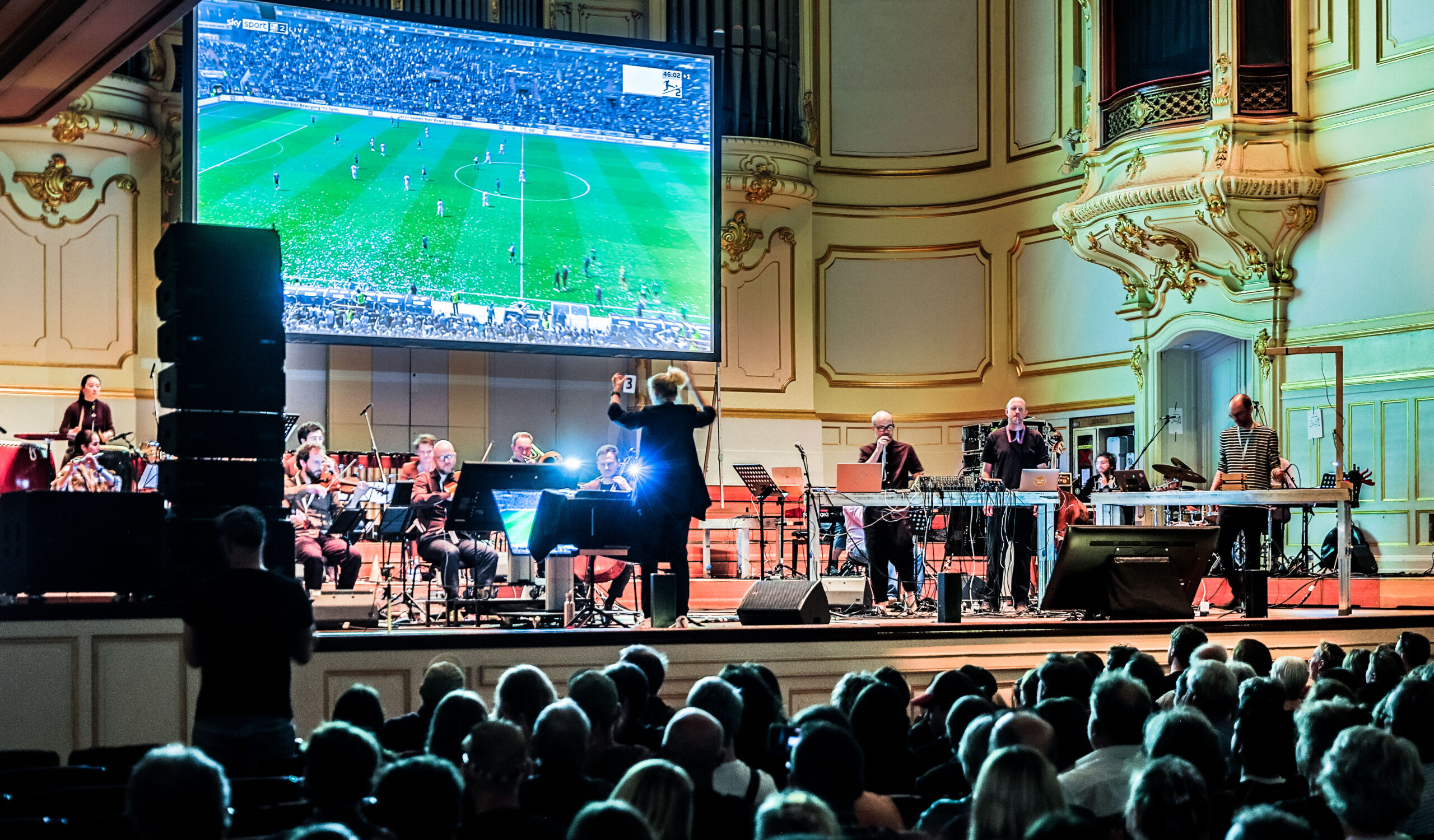 Großer Bildschirm mit Fußball auf der Bühne, davor Musiker