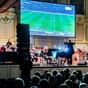 Großer Bildschirm mit Fußball auf der Bühne, davor Musiker