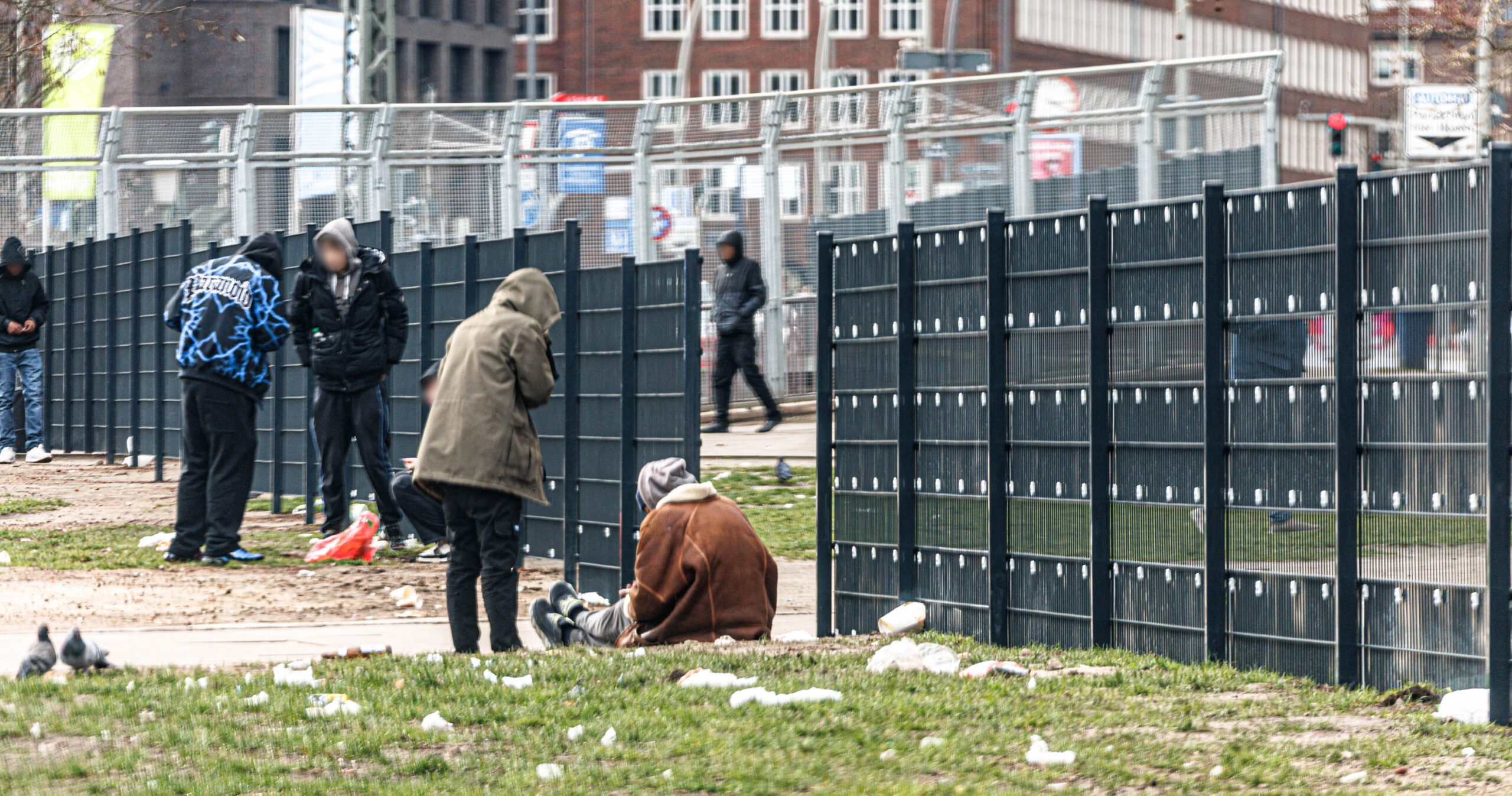 Menschen hocken vor einem Metallzaun auf dem Boden