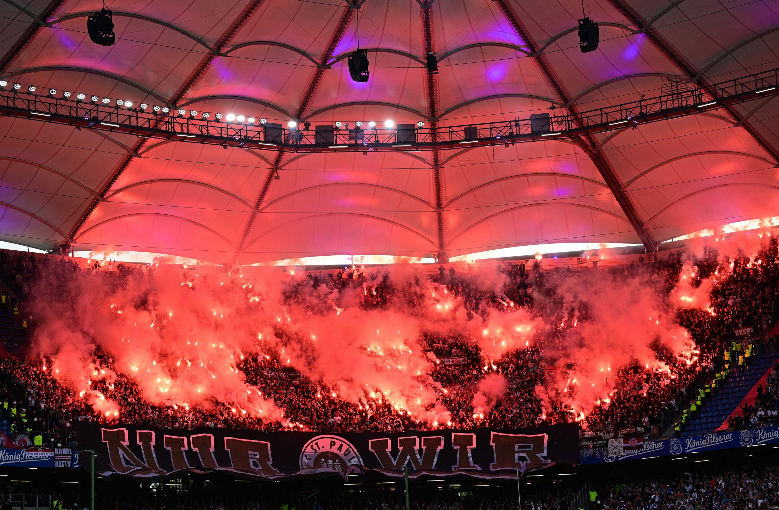 Die Gäste-Kurve mit den St. Pauli-Fans im Volksparkstadion ist von bengalischen Feuern rot erleuchtet