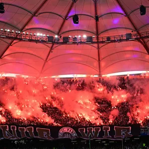 Die Gäste-Kurve mit den St. Pauli-Fans im Volksparkstadion ist von bengalischen Feuern rot erleuchtet