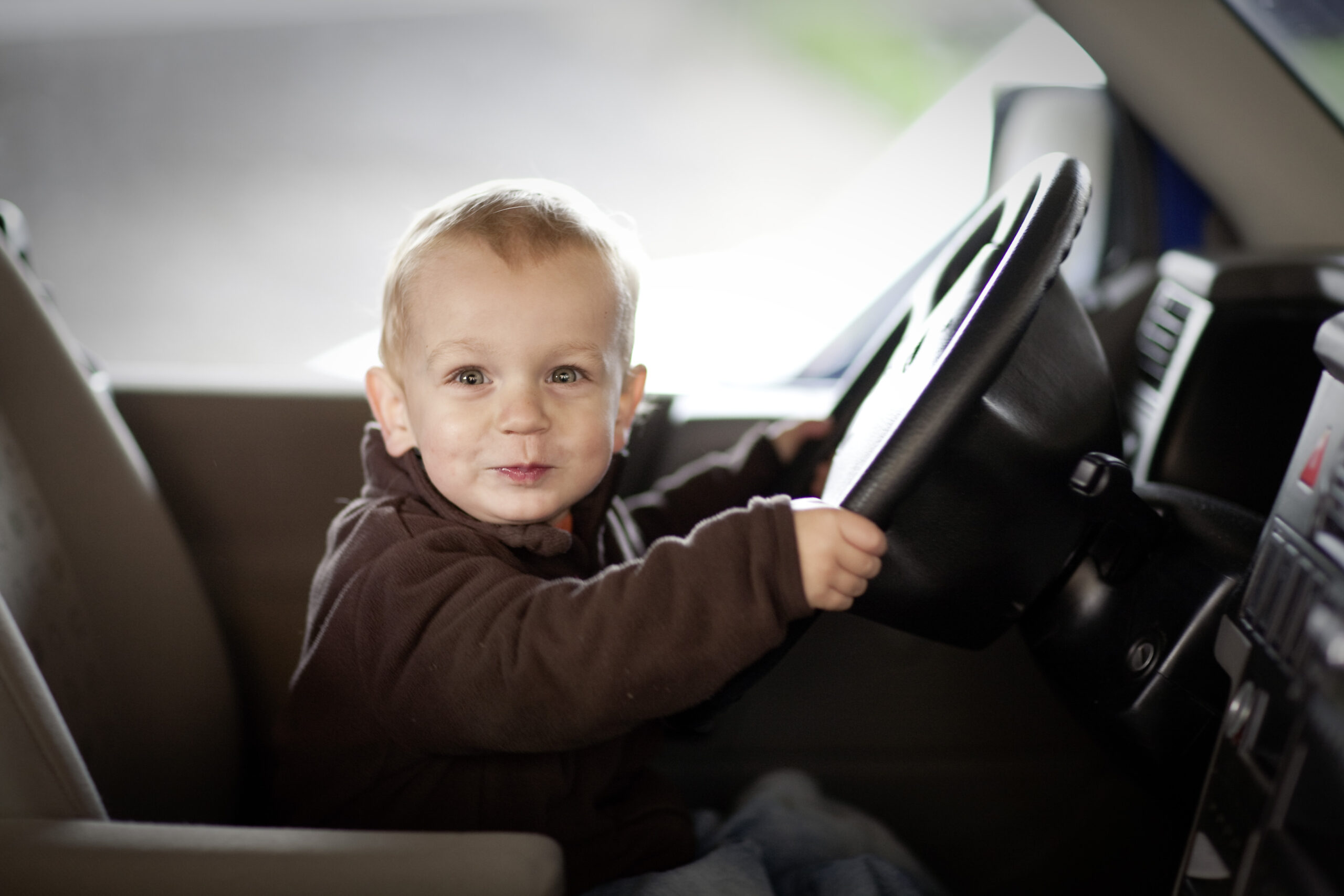 Ein kleiner Junge sitzt in einem Auto am Steuer.