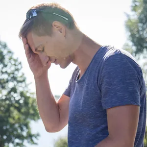 Ein Mann leidet wegen der Sonne unter Kopfschmerzen.
