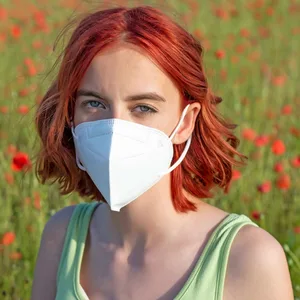 Eine Frau steht mit FFP2-Maske auf einer Wiese.