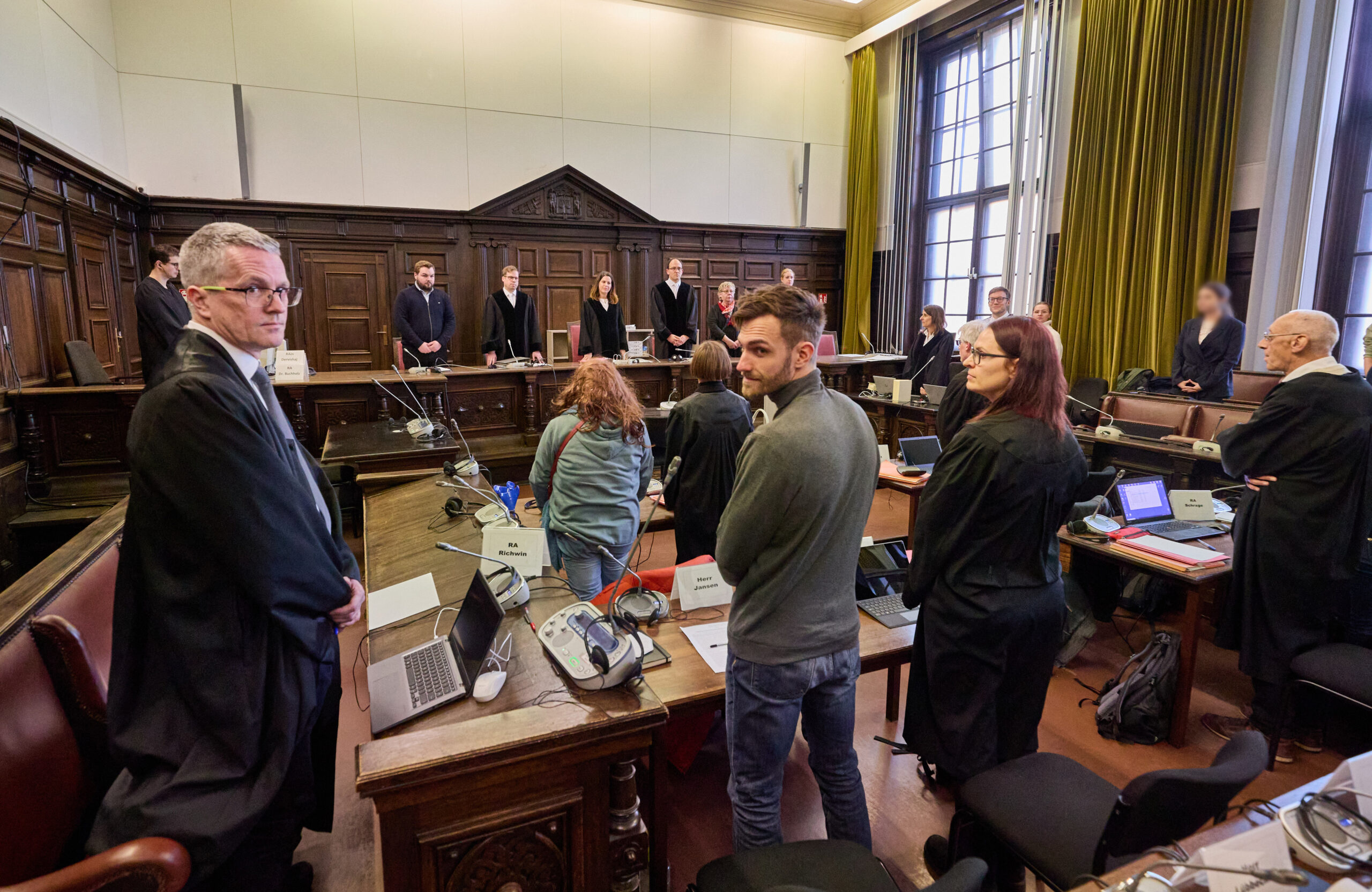 Der Angeklagte Nils J. (M.), die Richter, Anwälte sowie weitere Angeklagte stehen im Gerichtssaal