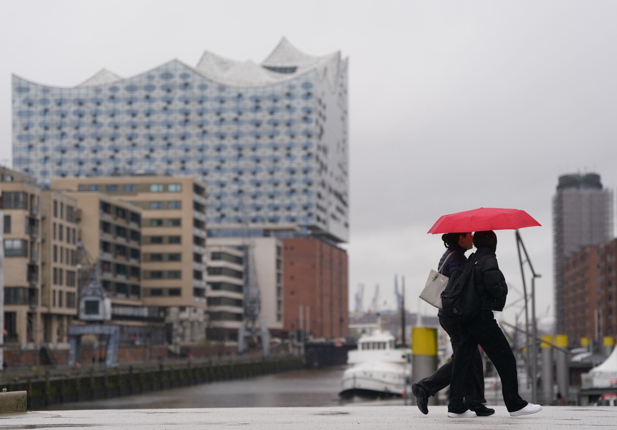 Zwei junge Frauen gehen mit einem roten Regenschirm im Dauerregen über die Magellan-Terrassen in der Hafencity.