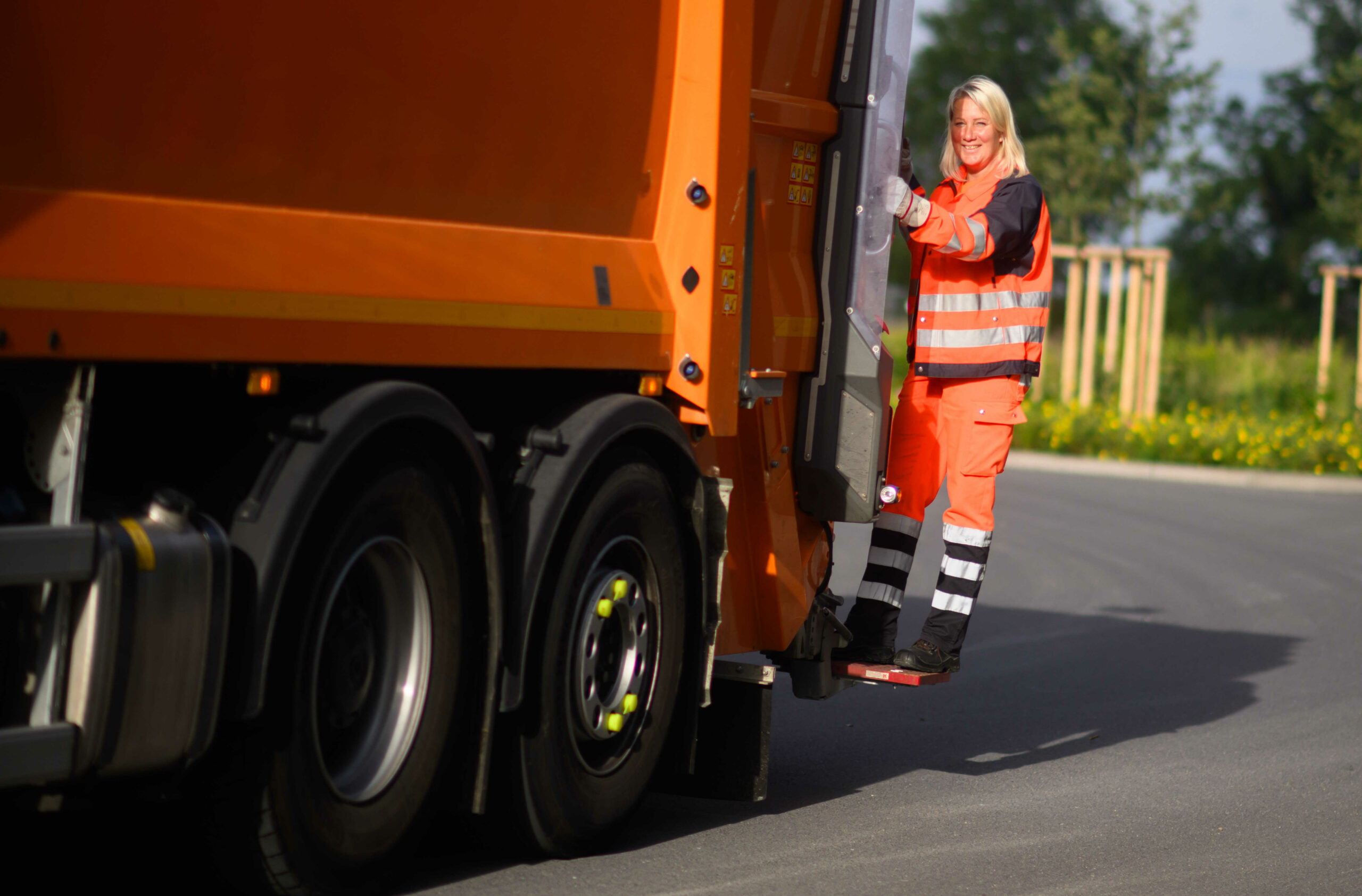 Müllwerkerin steht auf einem Müllfahrzeug.