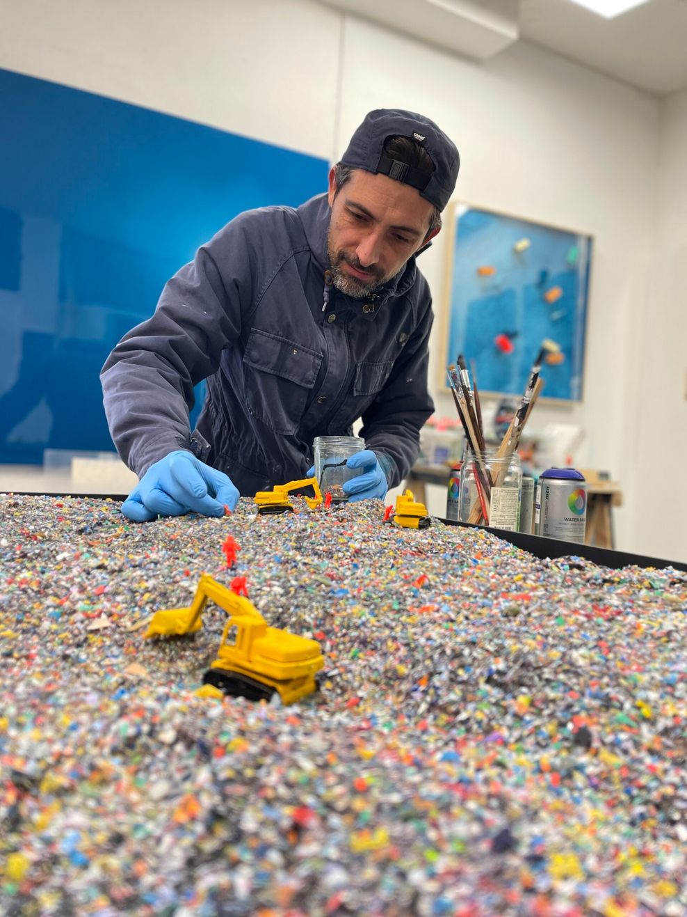 Mathieu Lucas bei der Arbeit an einer Miniaturbühne: Er platziert winzige Figuren auf einer Halde von geschredderten Plastikteilchen.