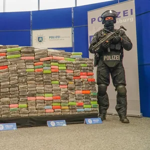 Zwei bewaffnete Polizisten stehen neben einer Palette, auf der sich sichergestellte Kokainpakete stapeln (Symbolfoto)