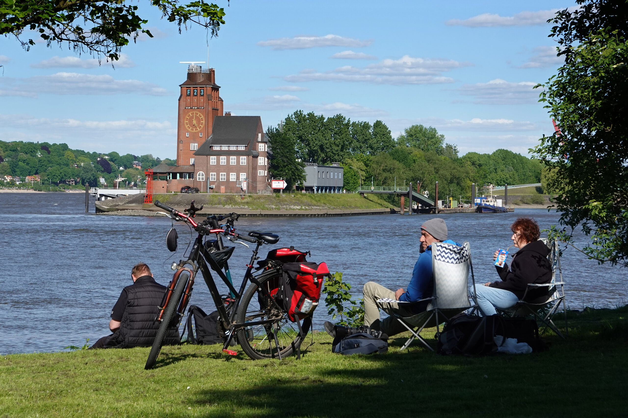 Drei Menschen sitzen im Gorch-Fock-Park in Finkenwerder und blicken auf die Elbe.