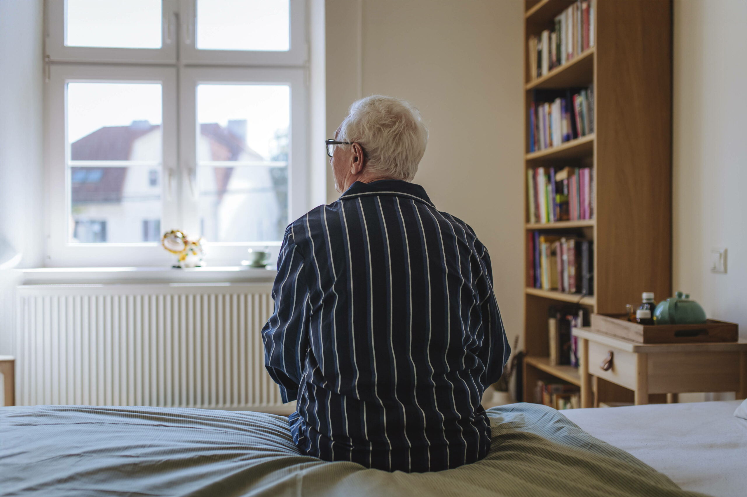 Alter Mann sitzt auf einem Bett.