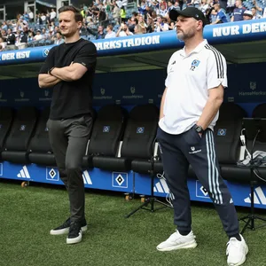 Steffen Baumgart und Claus Costa stehen am Spielfeldrand des Volksparkstadions nebeneinander und schazen auf den Platz