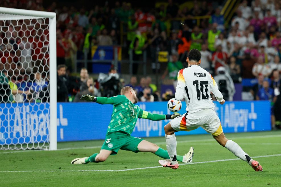 Jamal Musiala (vorne) schießt an Kasper Schmeichel vorbei.