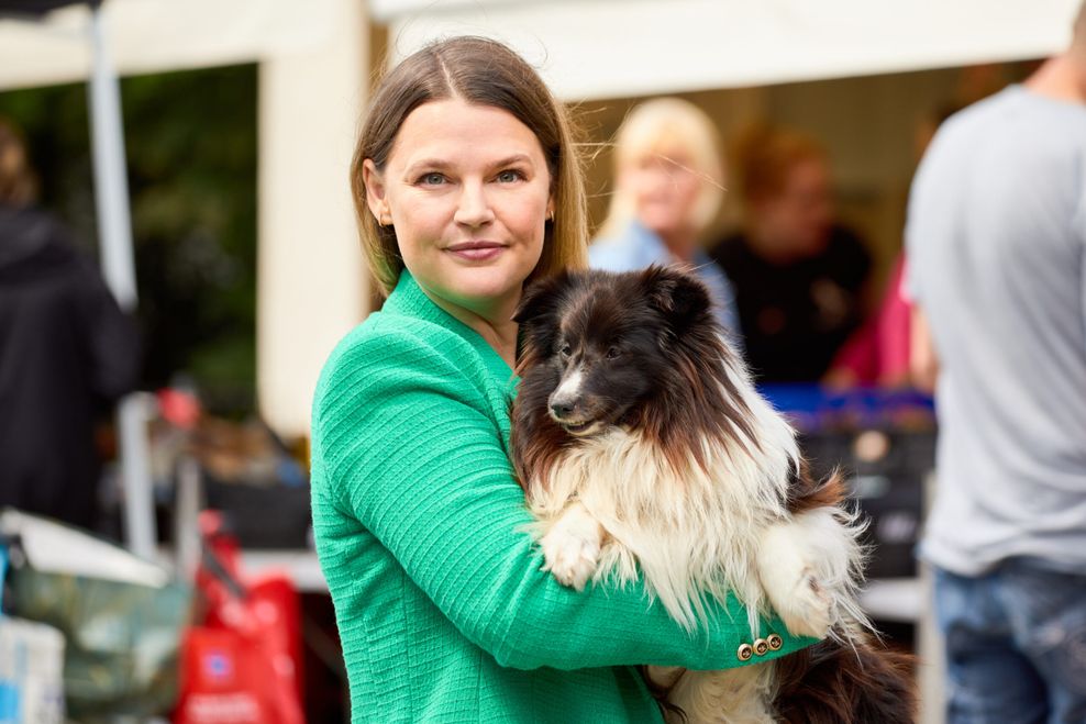 Junge Frau mit grünem Blazer und Hund auf dem Arm