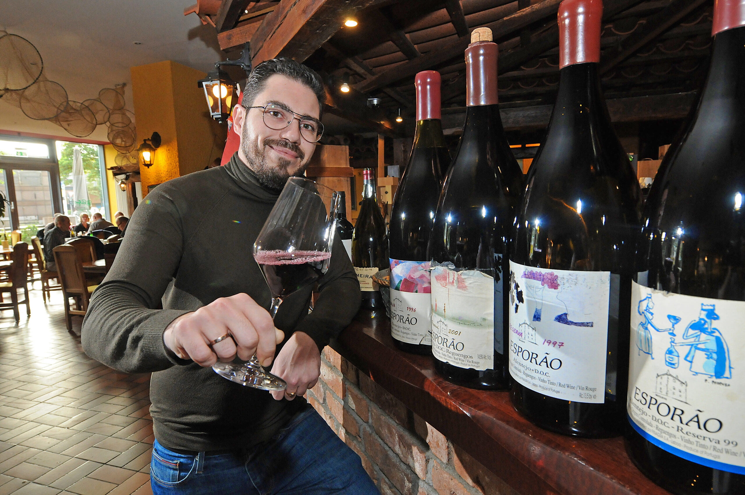 Junger Mann mit Brille hält ein Glas mit Rotwein