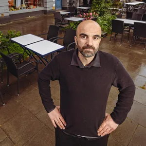 Mann steht auf einer Restaurantterrasse, Hände in die Hüften gestützt