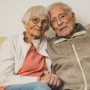 Altes Paar lehnt lächelnd die Köpfe aneinander