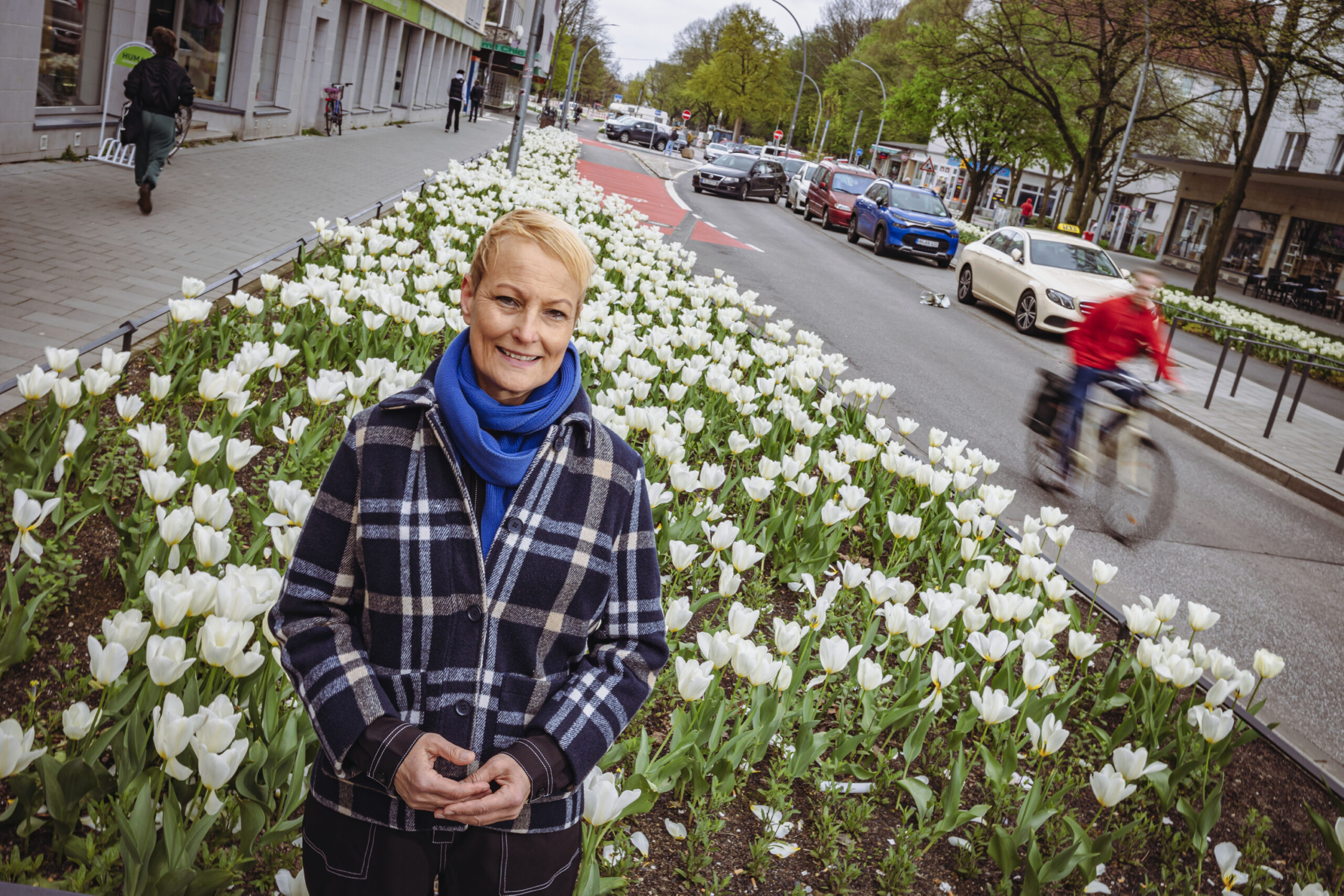 Frau mit kurzen blonden Haaren vor Blumenbeet