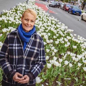 Frau mit kurzen blonden Haaren vor Blumenbeet