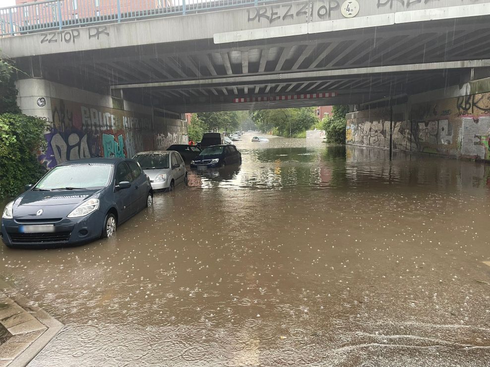 Die Straße an der Station Alte Wöhr ist überflutet. Im Hintergrund ist zu sehen, wie ein parkendes Auto wegschwimmt.