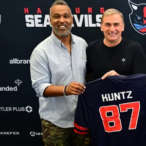 Patrick Esume, Stefan Kuntz, Mark Weitz und Miguel Boock halten ein Sea-Devils-Trikot und lachen in die Kamera