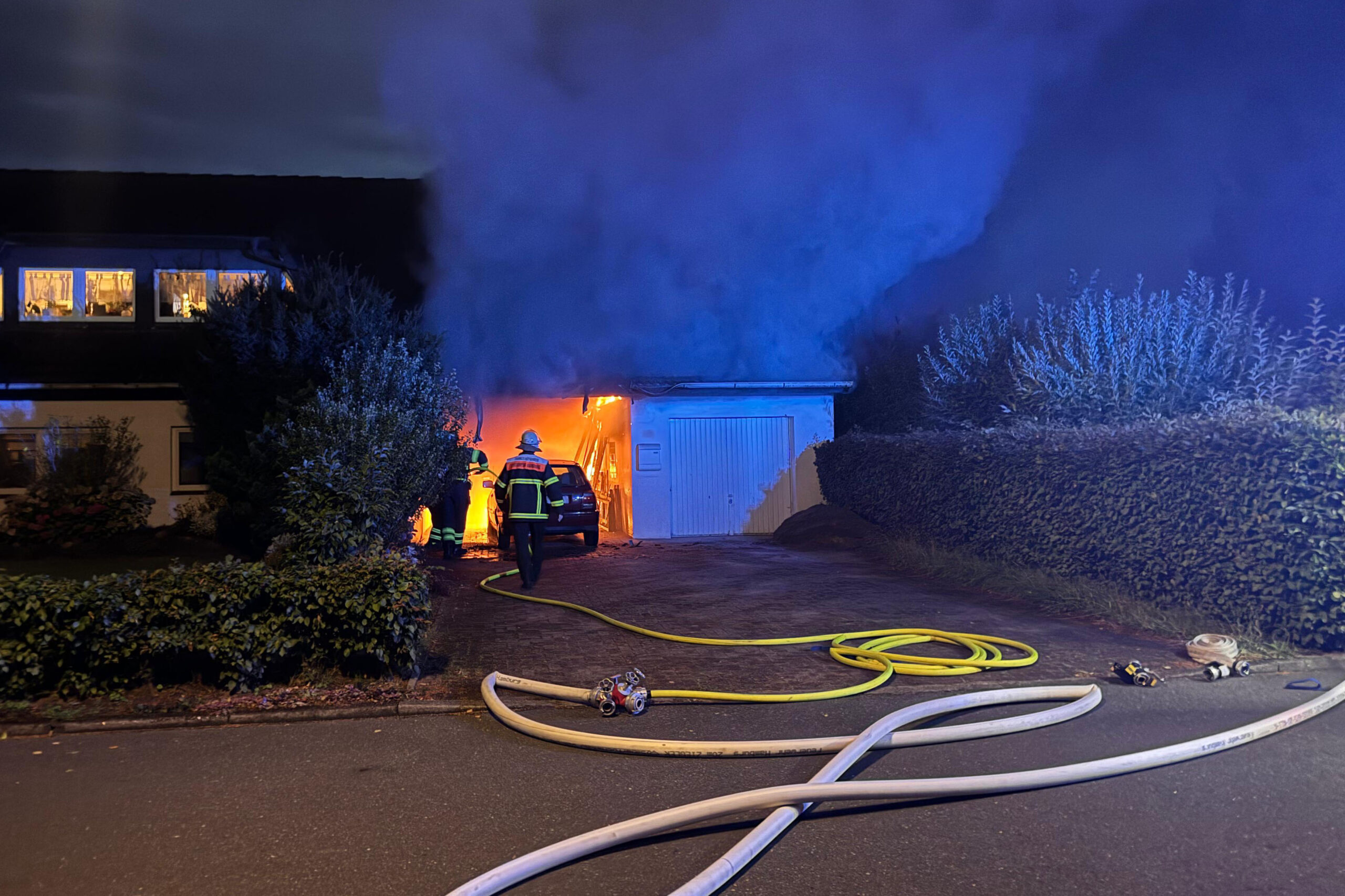 Feuerwehrleute stehen vor dem brennenden Carport.