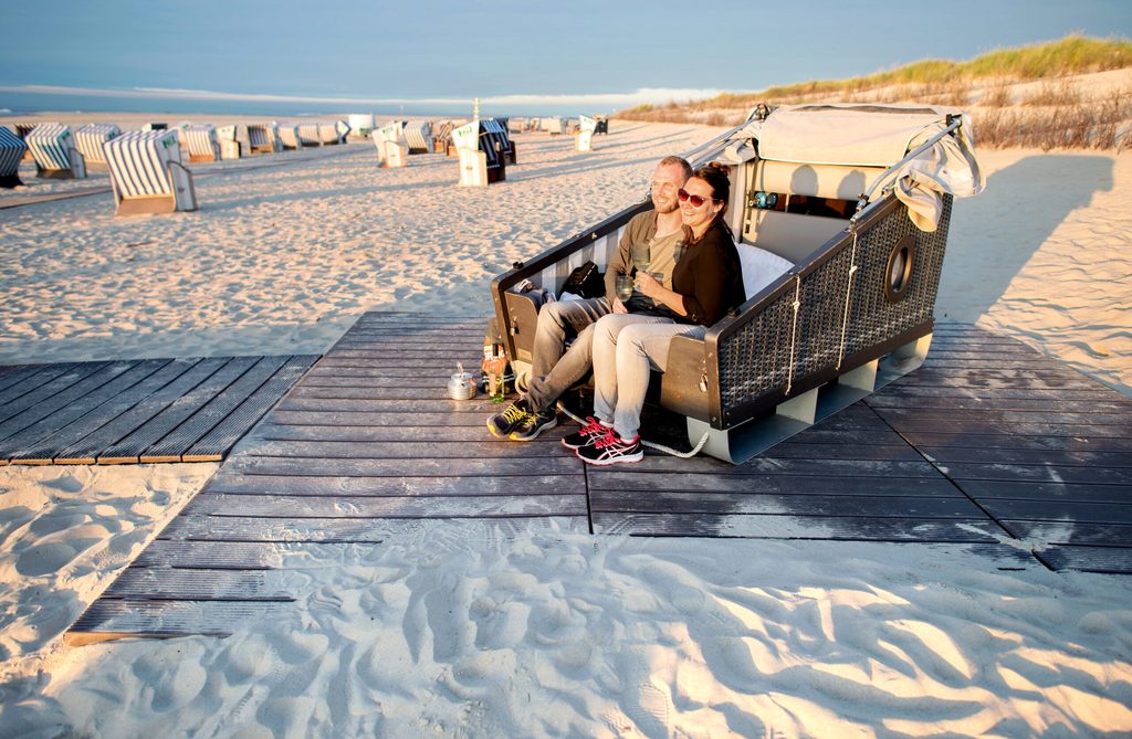 Zwei Menschen sitzen in einem Schlafstrandkorb am Strand.