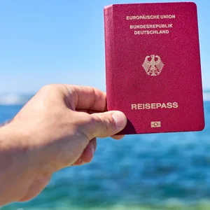 Ein Tourist hält einen deutschen Reisepass vor das Meer im Urlaub.
