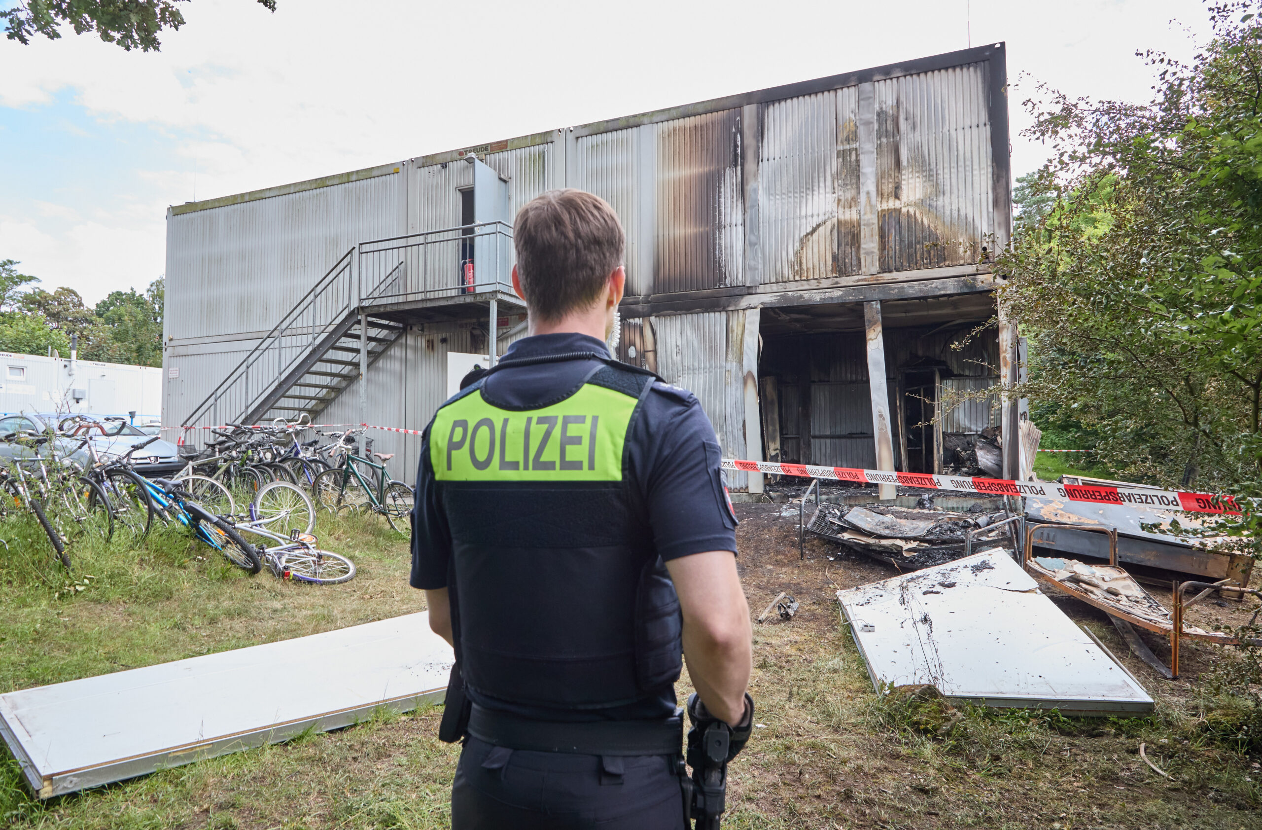 Ein Polizist steht vor den Wandteilen, die nach einer Explosion in einer Asylbewerberunterkunft in Buchholz vor den Wohncontainern liegen. Ein Mensch starb, ein Polizist wurde schwer verletzt.