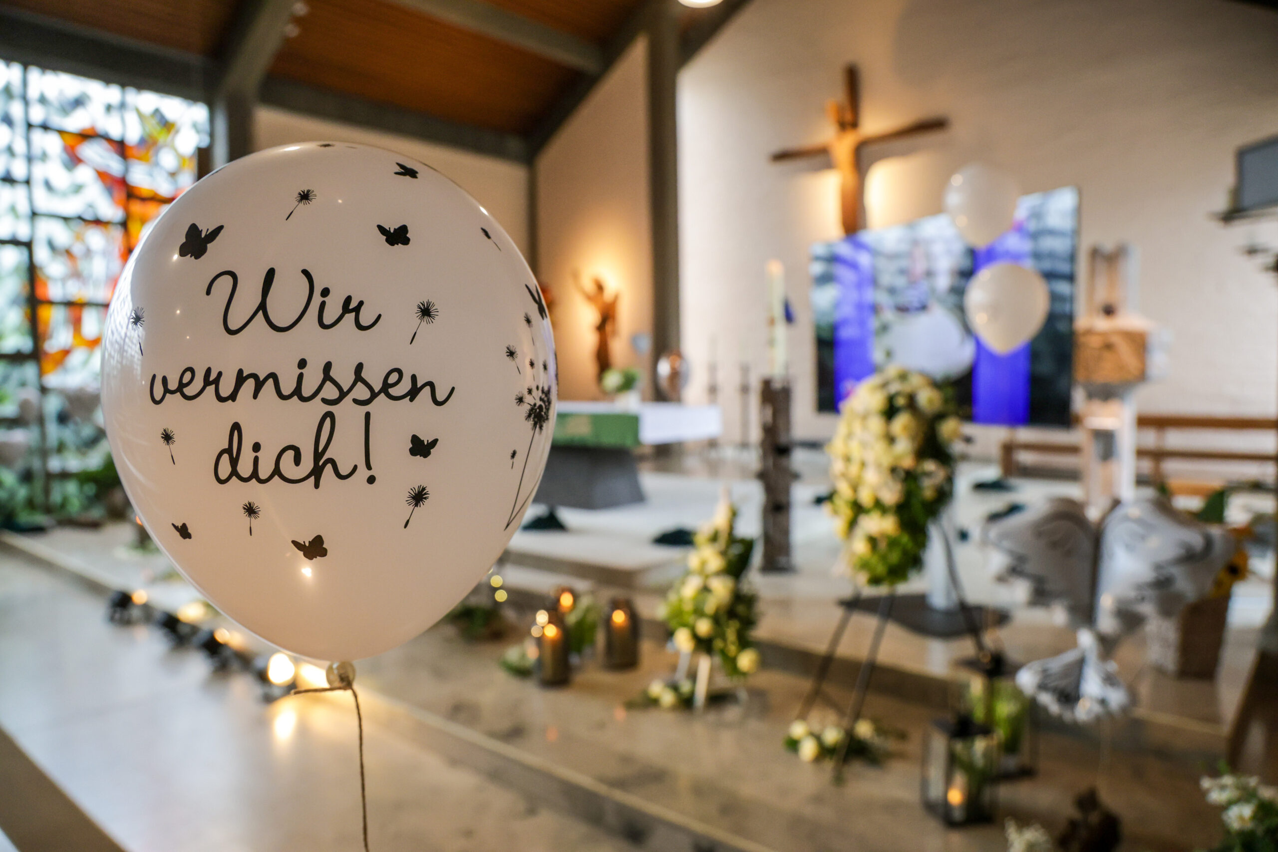 Ein Luftballon mit der Aufschrift „Wir vermissen dich!“ schwebt vor dem geschmückten Altarraum der katholischen St. Michael Kirche