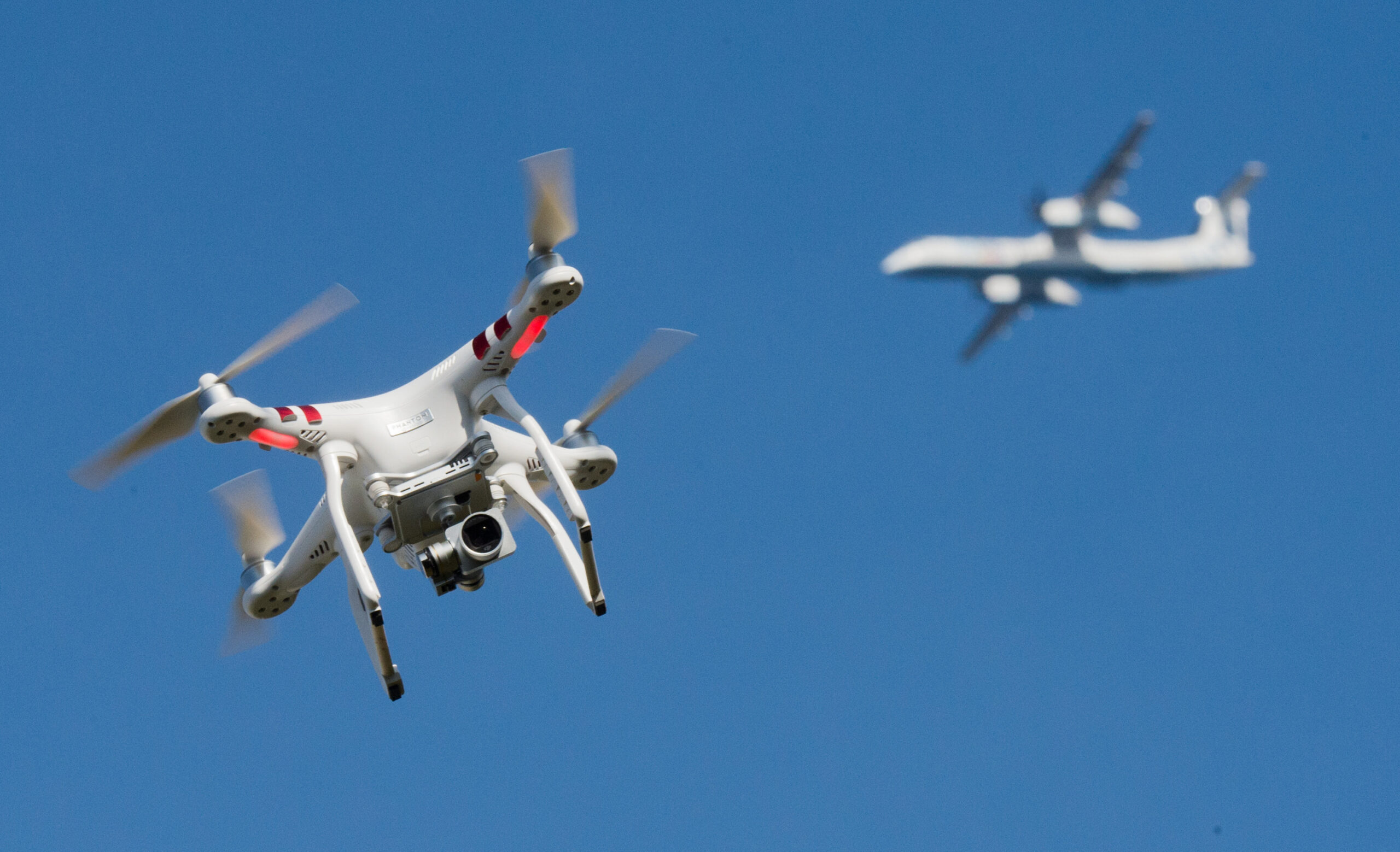 Eine private Drohne fliegt in weiter Entfernung von einem Flugzeug.